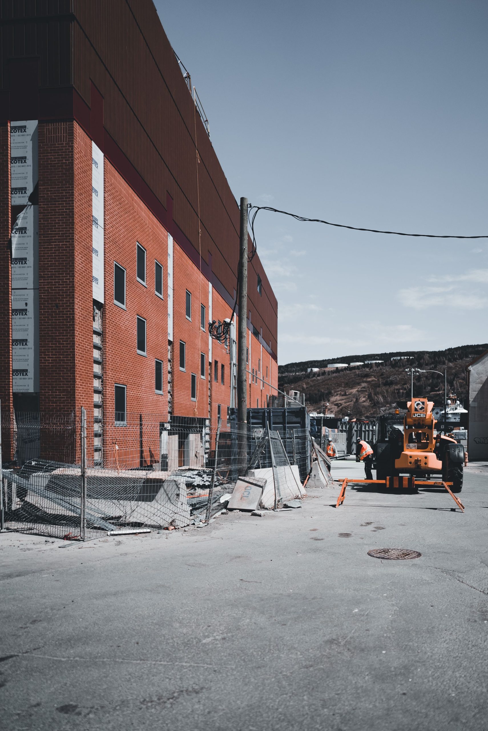 Industrial scene of a brick building under construction with machinery and safety fences.