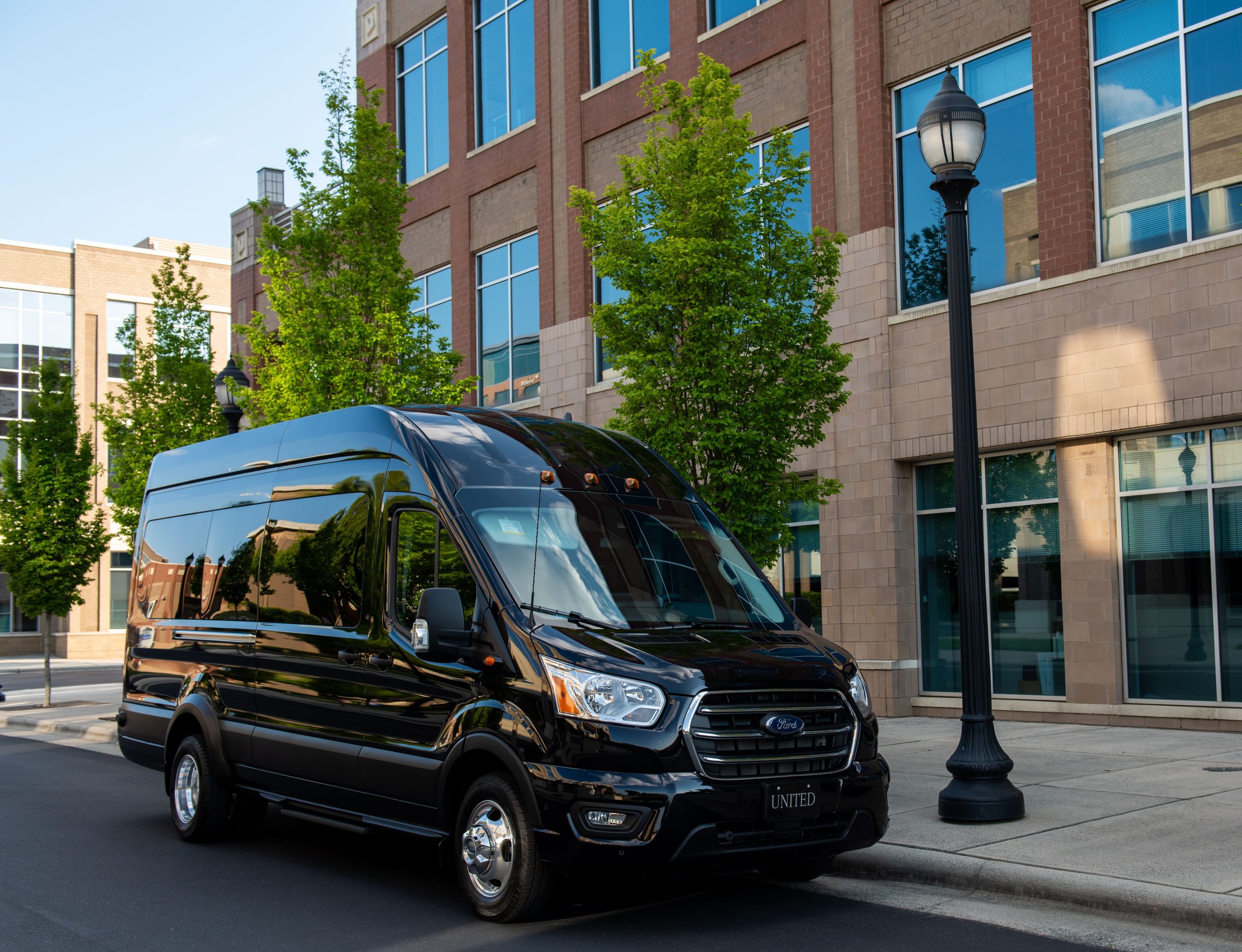 A sleek black van parked on a city street by a modern office building.